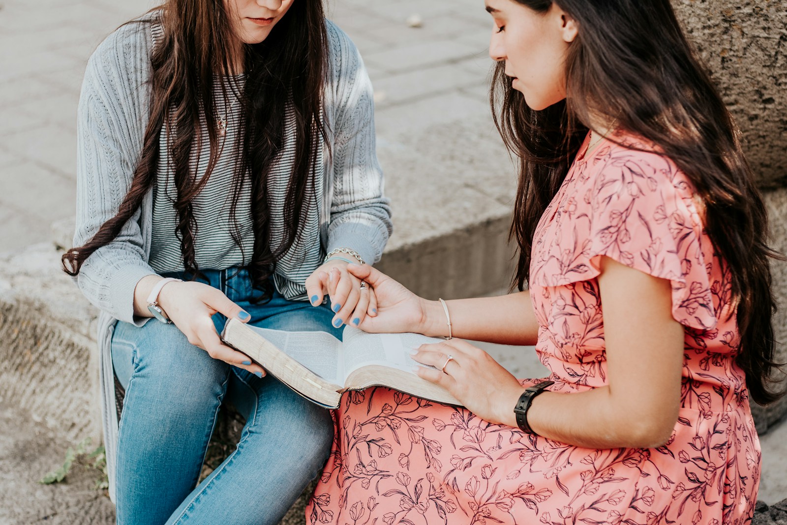 woman in white and black striped long sleeve shirt and blue denim jeans sitting on concrete